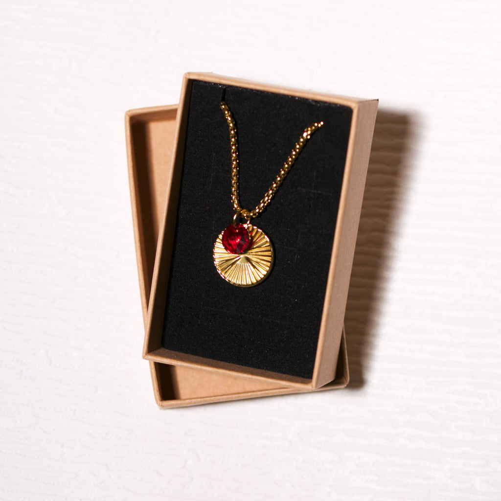 Gold necklace with a red gemstone in a black jewelry box on a white background
